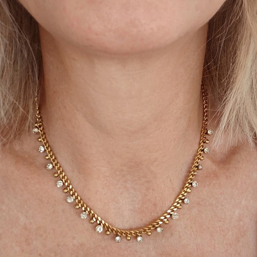 Gold-tone necklace with dangling clear stones and small beads worn around the neck.