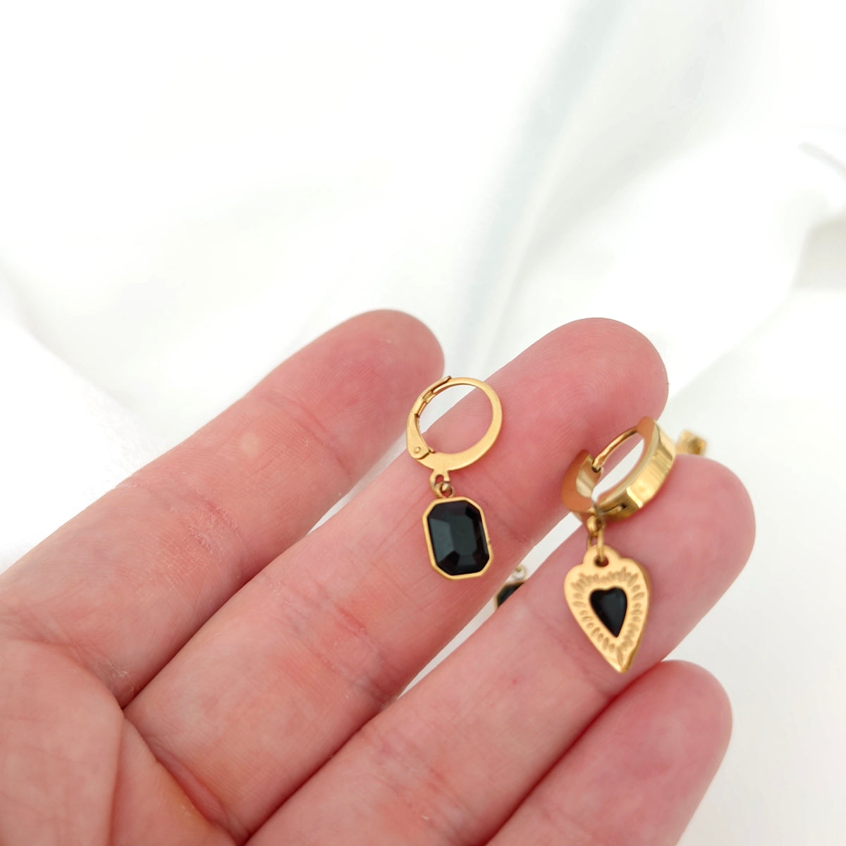 Two gold-tone hoop earring designs with black rectangular and heart charms