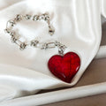 Silver-tone chain bracelet with a deep red heart charm on white satin.
