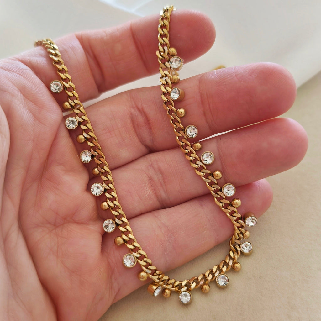 Close-up of gold-tone necklace with dangling clear stones and small beads held in a hand.