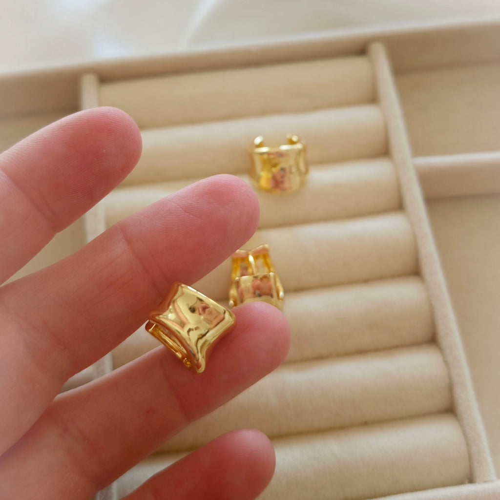 Close-up of a polished gold-tone curved hoop earring held in a hand.