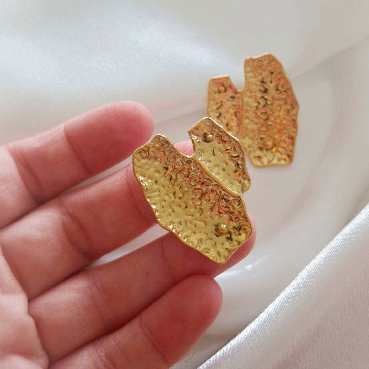 Close-up of a gold-tone textured folded earring held in a hand.