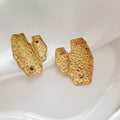 Pair of gold-tone earrings with irregular folded shapes and textured surfaces on ivory satin.