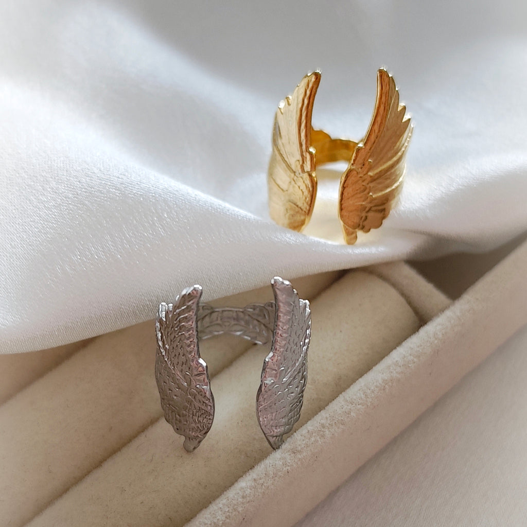Silver-tone and gold-tone steel wing rings on ivory fabric.