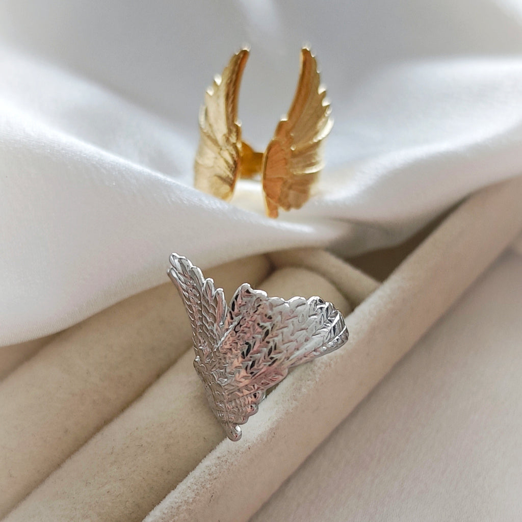 Detailed silver-tone wing ring with a gold-tone wing ring in the background.