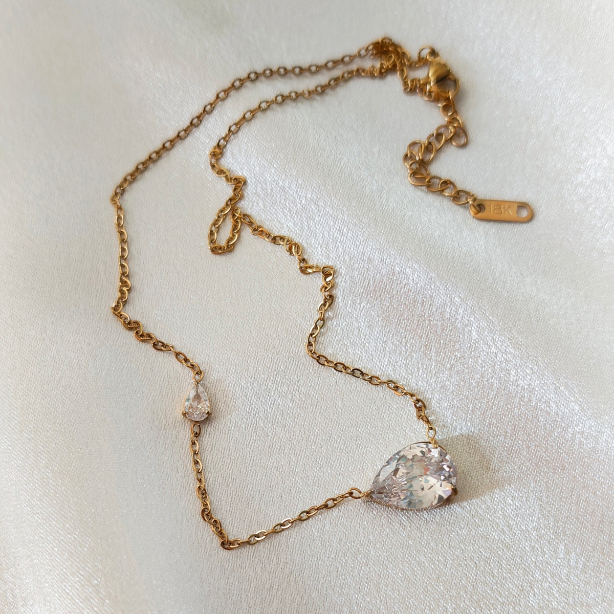 Gold-tone necklace with two clear teardrop-shaped stones on ivory fabric.
