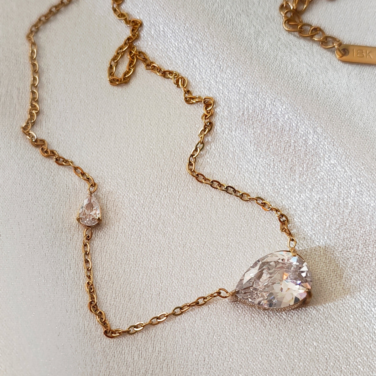 Gold-tone asymmetrical necklace with a large and a small clear teardrop stone.