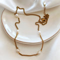 Gold-tone steel necklace with white beads displayed on a white plate.