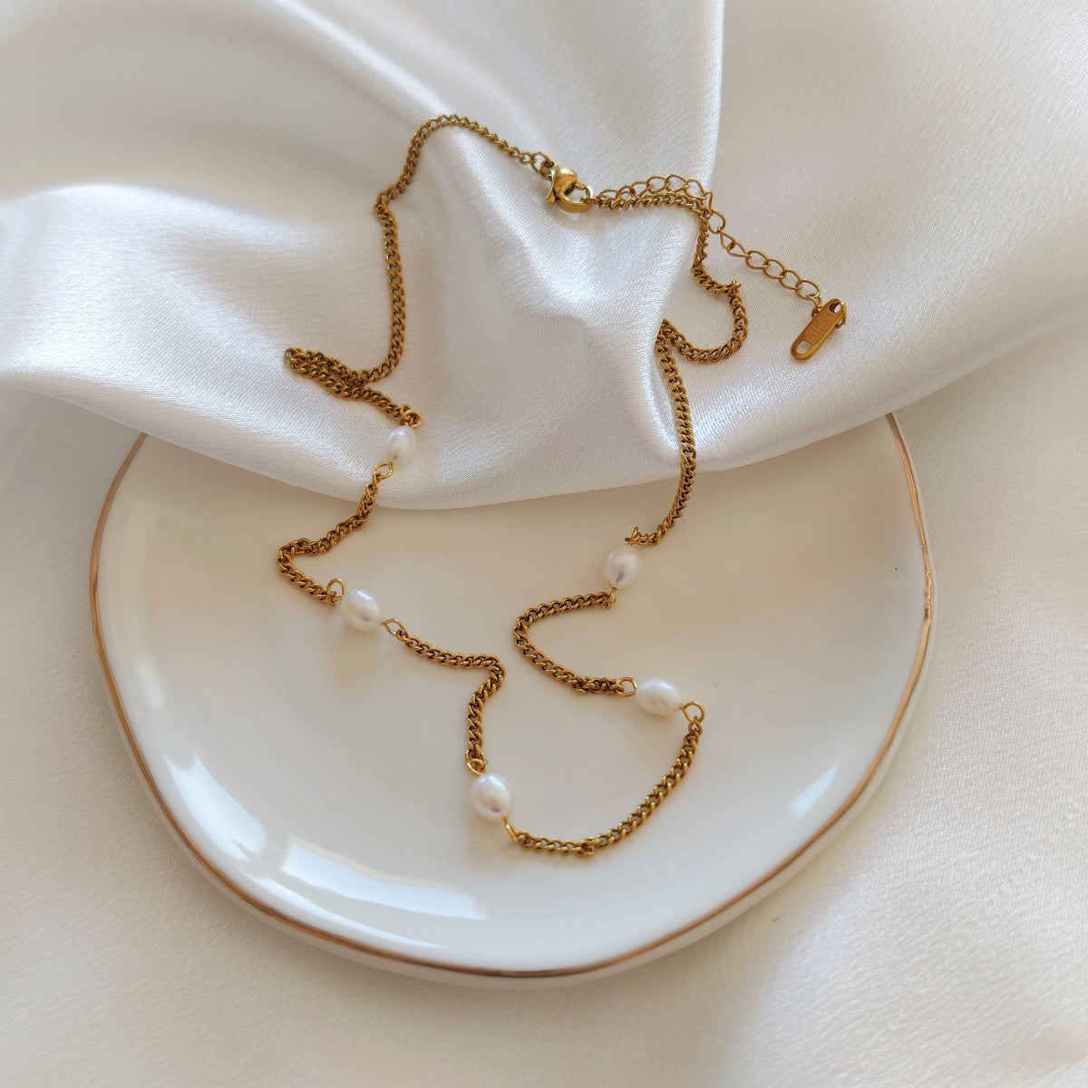 Gold-tone necklace with white beads and extension chain on satin and a plate.