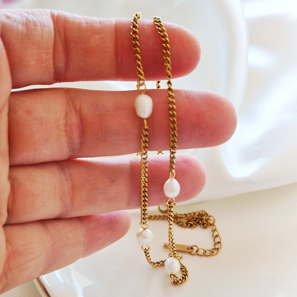 Close-up of gold-tone steel necklace with white beads held in a hand.