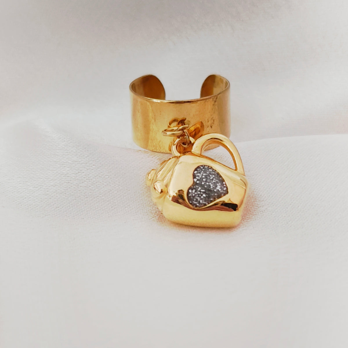 Gold-tone mug charm ring with a sparkling heart worn on a hand.