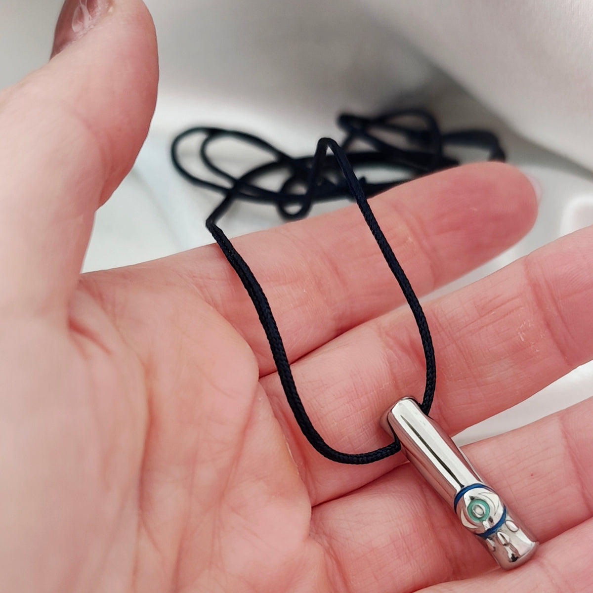 Close-up of a silver-tone steel eye pendant on black cord held in a hand.
