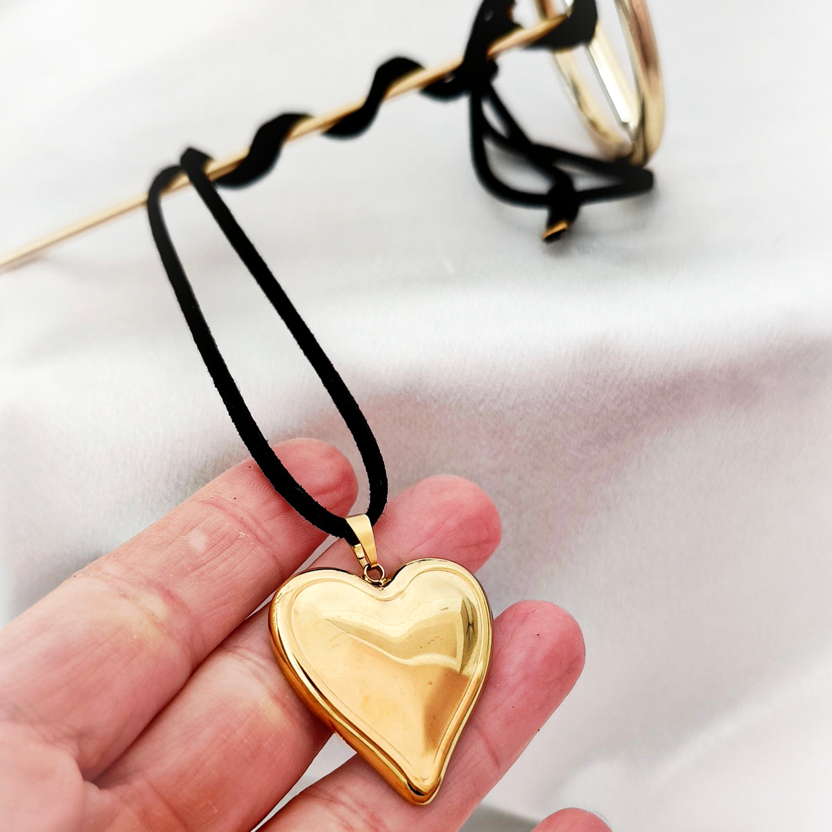 Gold-tone steel heart necklace with black suede cord held in a hand.