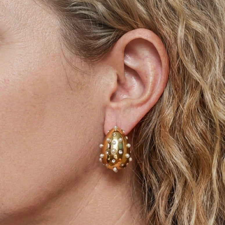 Gold-tone stainless steel teardrop earring with white bead details and sparkling accents, worn on the ear