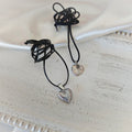Two heart pendant necklaces with black leather cords, one ribbed stainless steel heart and one silver-plated heart with wavy engravings
