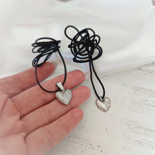 Close-up of ribbed stainless steel and engraved silver-plated heart pendants on black leather cords