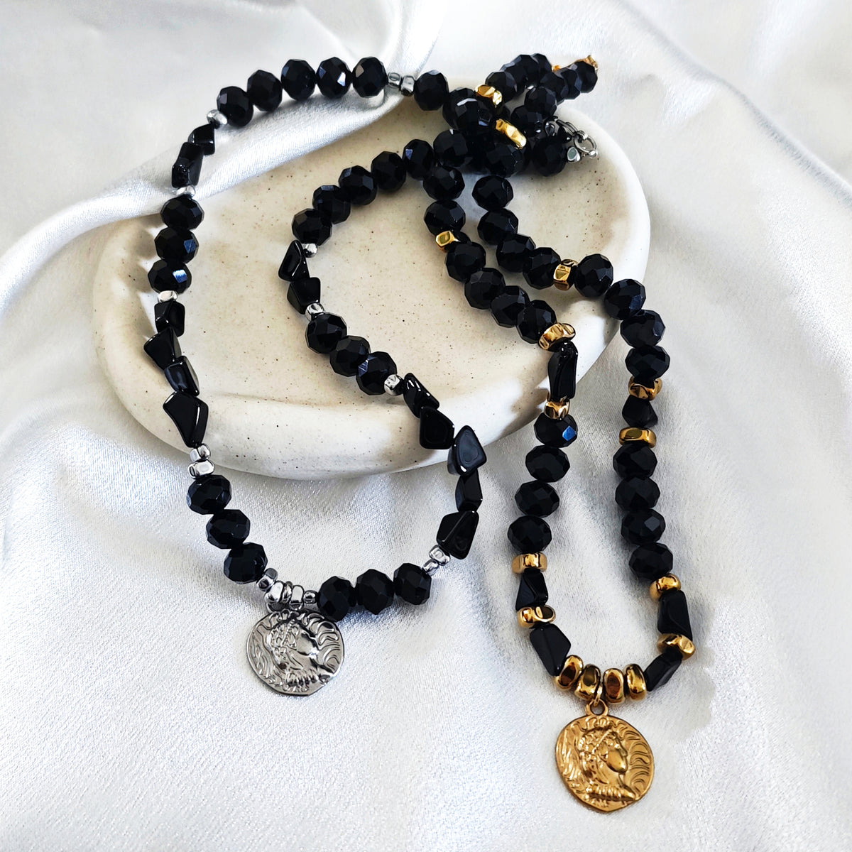 Black beaded necklaces with hematite, crystals and coin pendants in gold and silver tones.