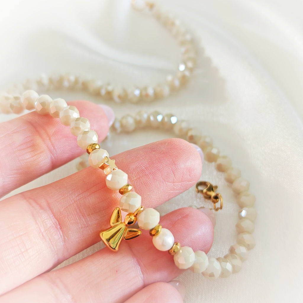 Close-up of ivory crystals, pearl and gold-plated angel charm held in hand.