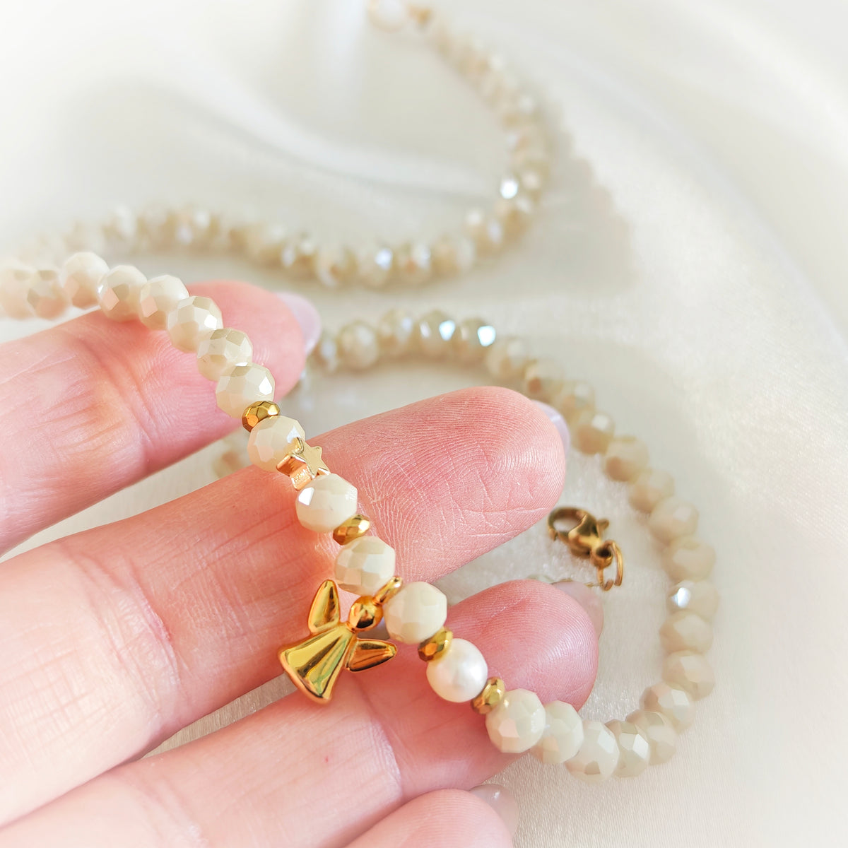 Close-up of ivory crystals, pearl and gold-plated angel charm held in hand.