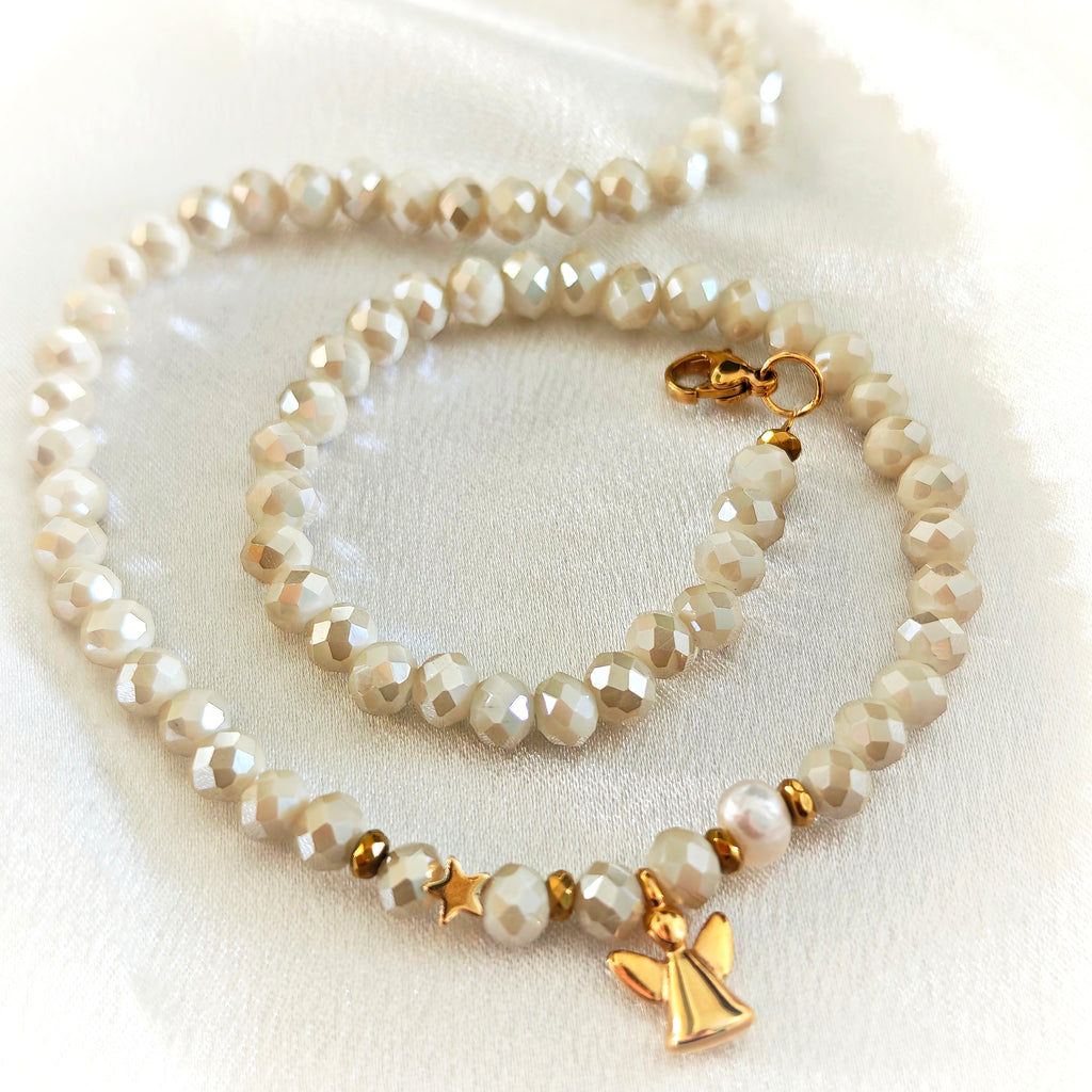 Ivory crystal necklace with pearl accents and gold-plated angel and star charms on white fabric.