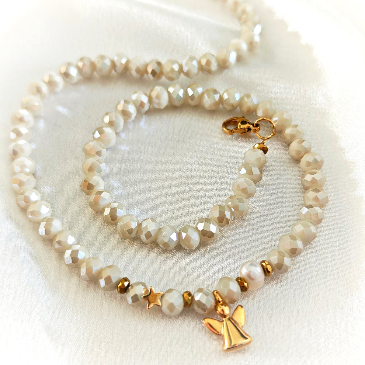 Ivory crystal necklace with pearl accents and gold-plated angel and star charms on white fabric.