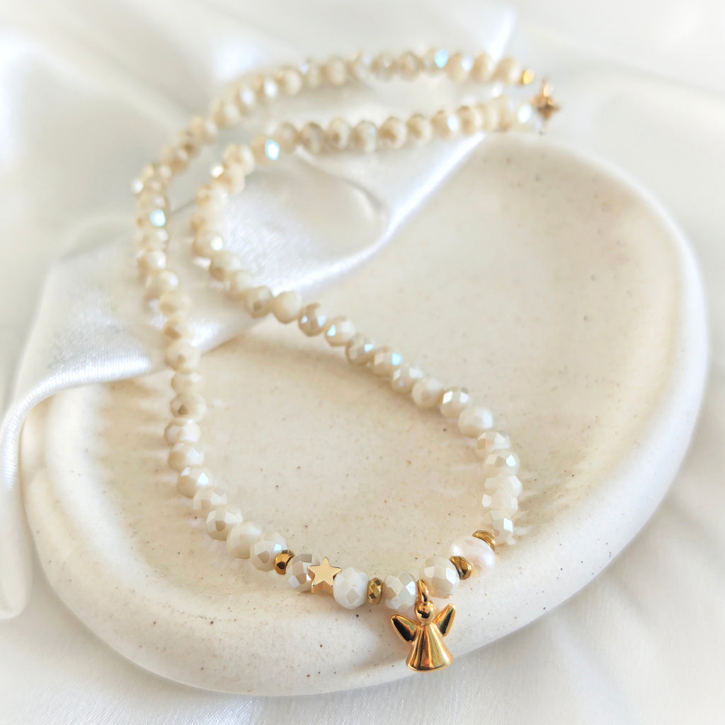 Ivory crystal and pearl necklace with gold-plated angel and star charms on a ceramic tray.