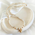 Ivory crystal and pearl necklace with gold-plated angel and star charms on a ceramic tray.