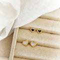 Mini heart stud earrings with gold-tone outlines and black or white centers on a beige jewelry tray