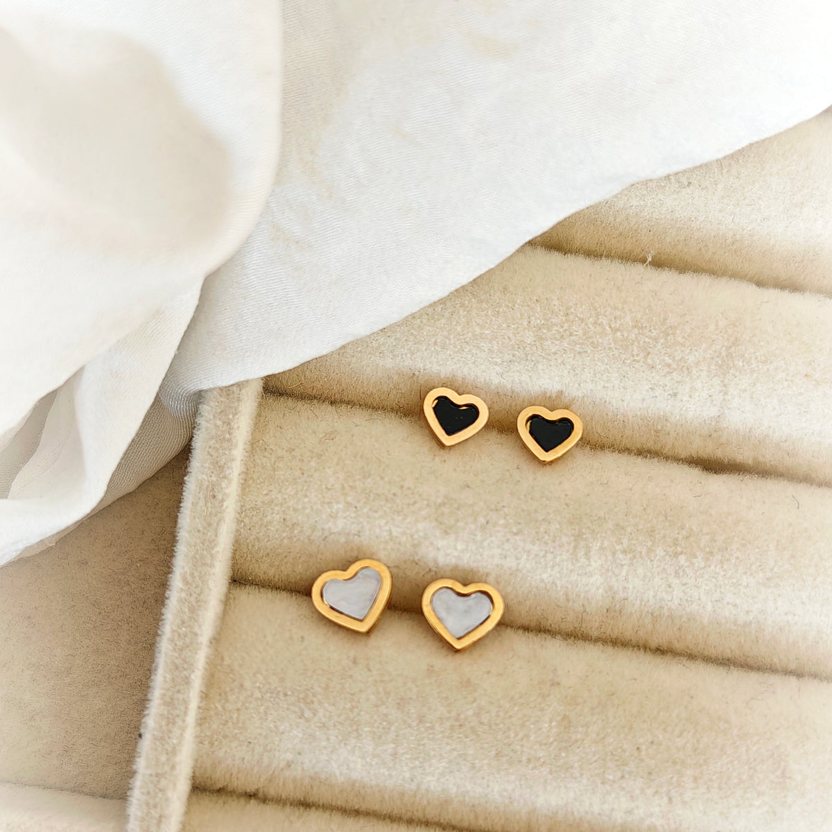 Mini heart stud earrings with gold-tone outlines and black or white centers on a beige jewelry tray