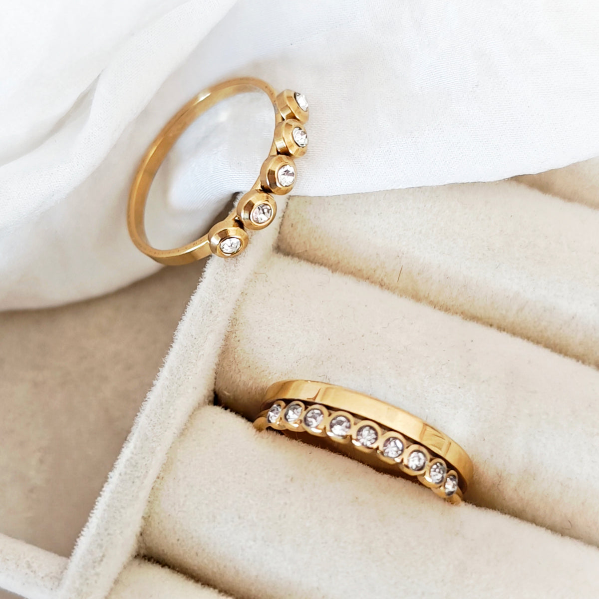 Two gold-tone steel rings with clear decorative stones, one with five spaced settings and one with a row of stones.