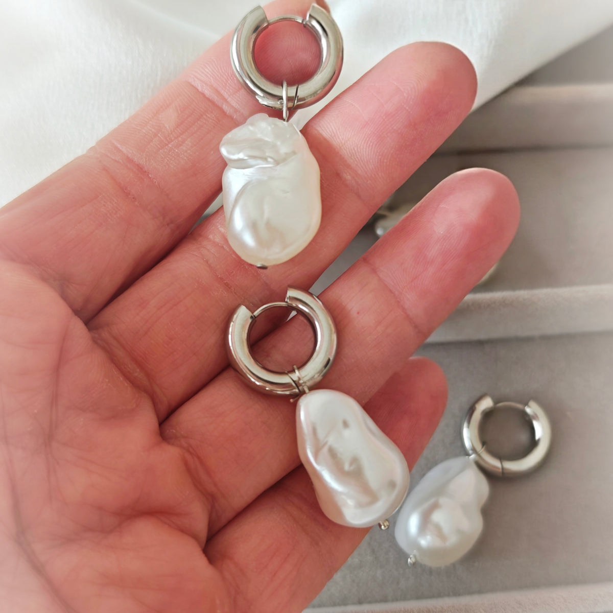Close-up of silver-tone hoops with white irregular pearlescent drops held in a hand