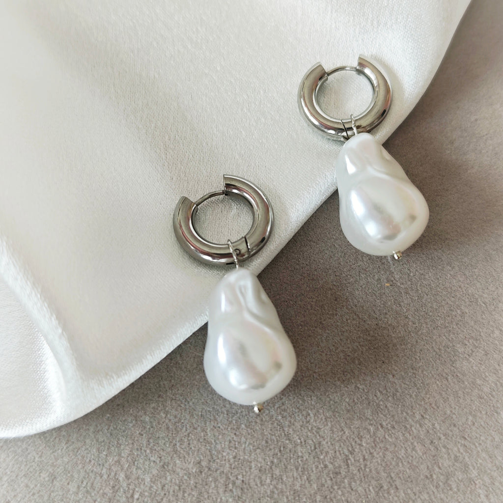 Two pairs of silver-tone hoop earrings with white pearlescent drops on a beige jewelry tray