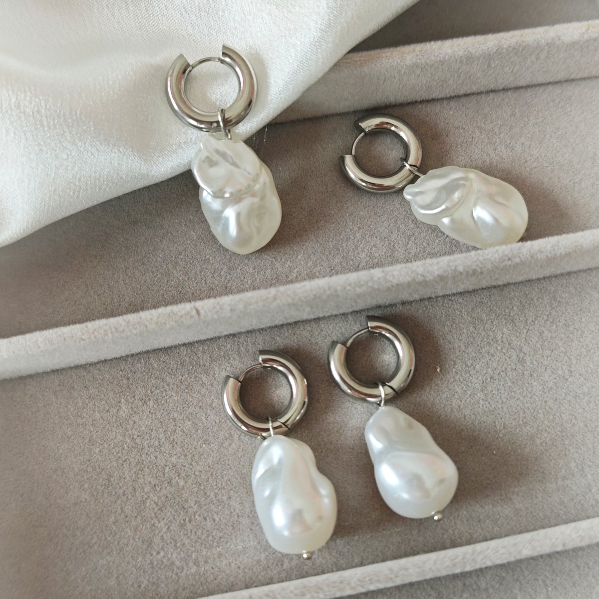 Silver-tone hoop earrings with white irregular pearlescent drops on white fabric