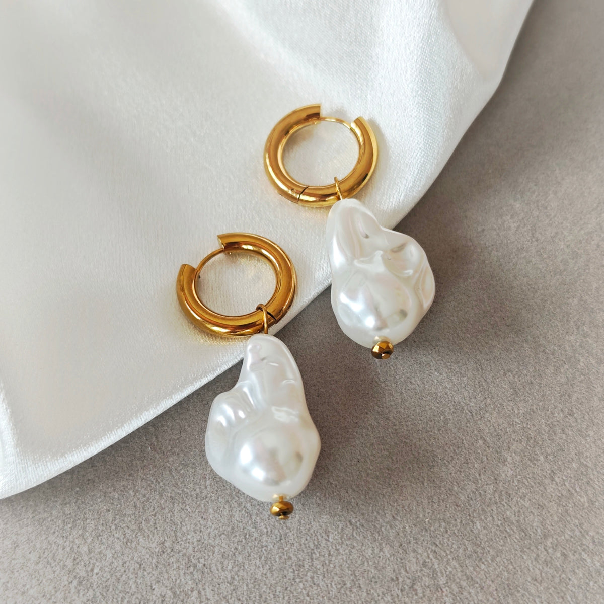 Gold-tone hoop earrings with white pearl drops on a beige jewelry tray