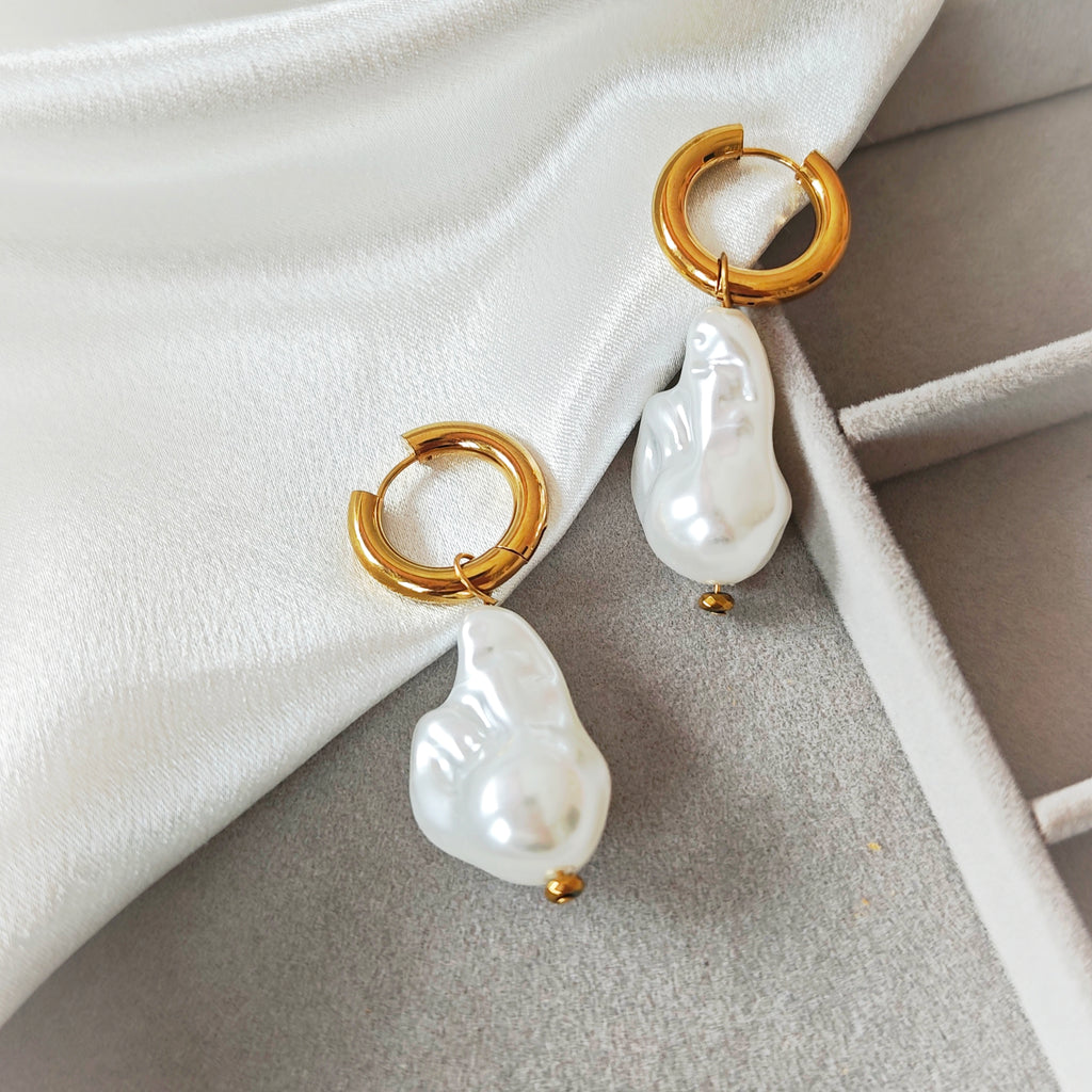Gold-tone hoop earrings with irregular white pearl drops on white fabric