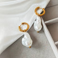 Gold-tone hoop earrings with irregular white pearl drops on white fabric