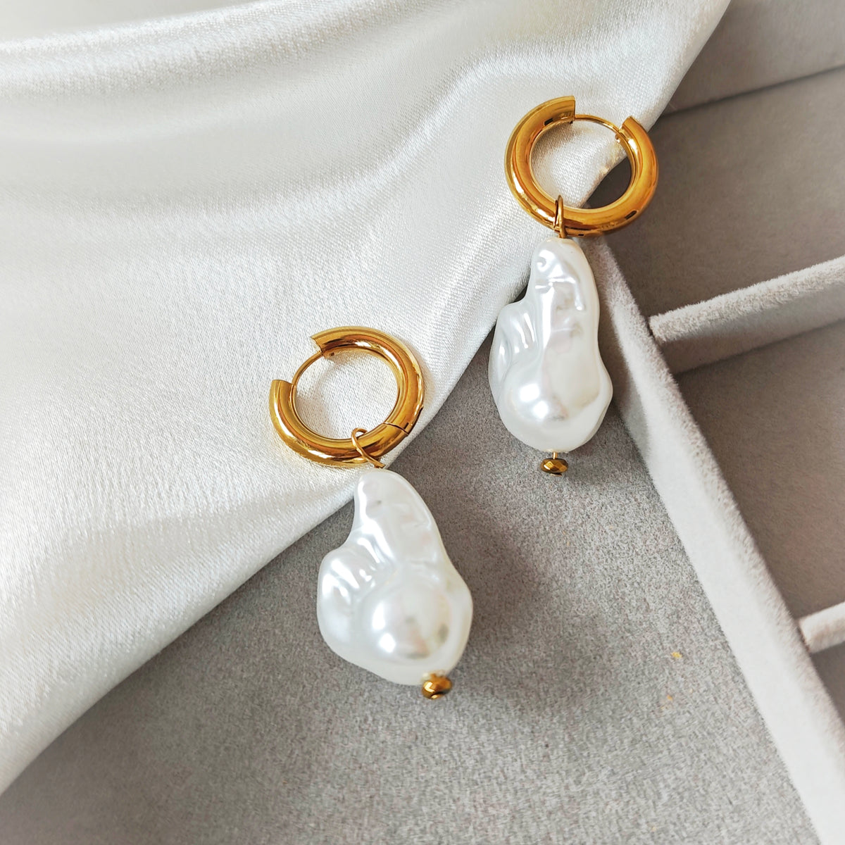 Gold-tone hoop earrings with irregular white pearl drops on white fabric