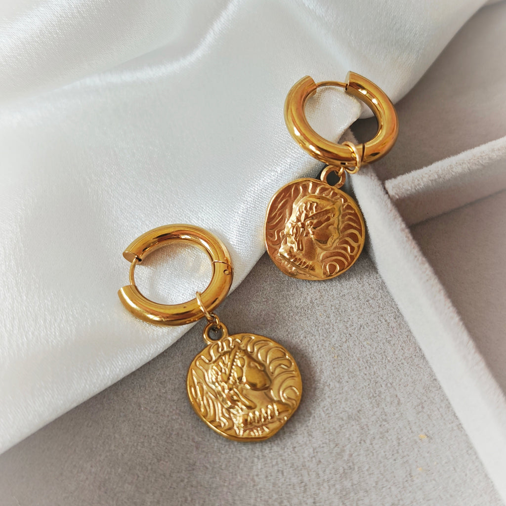 Gold-tone chunky hoop earrings with embossed coin charms on white fabric