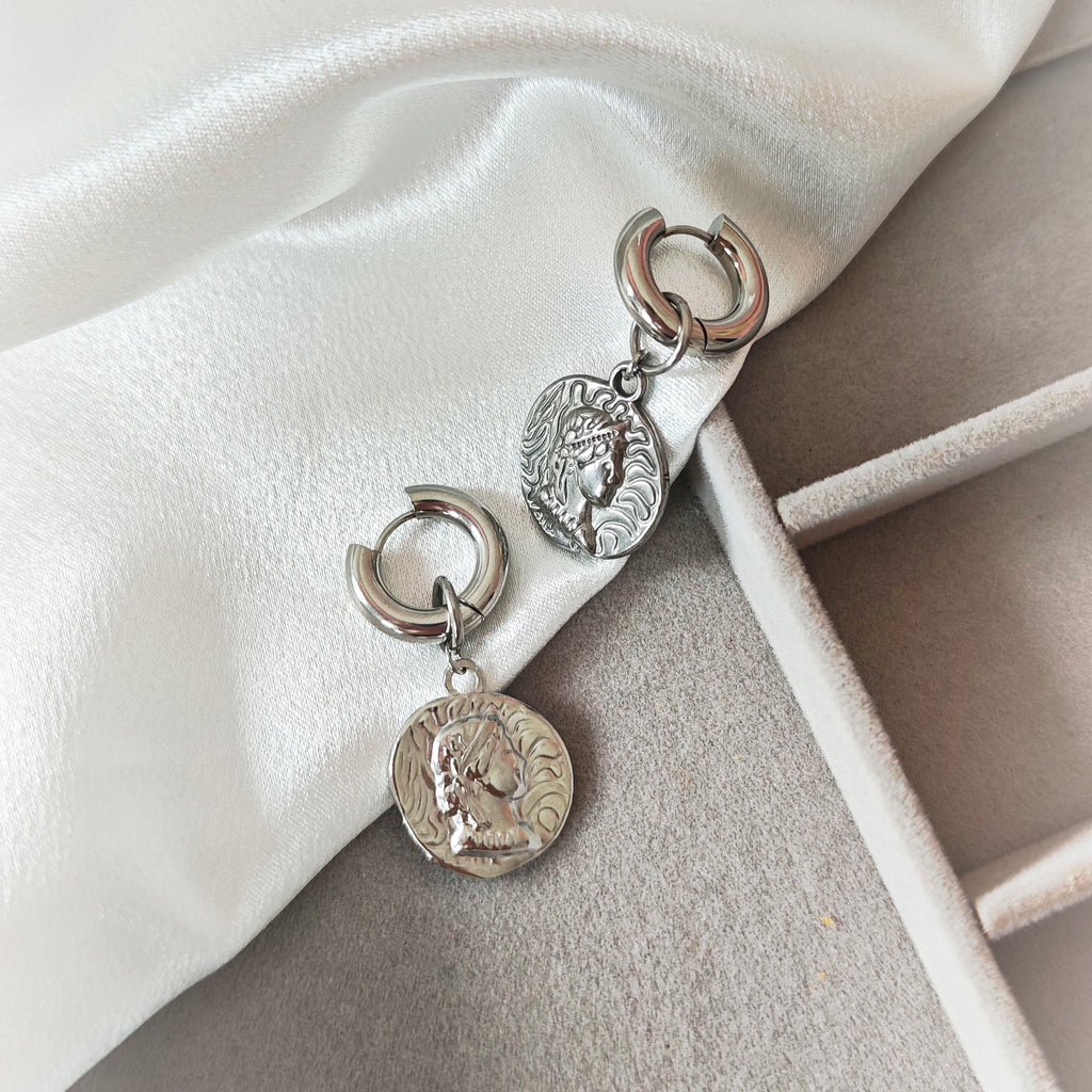 Silver-tone chunky hoop earrings with embossed coin charms on white fabric