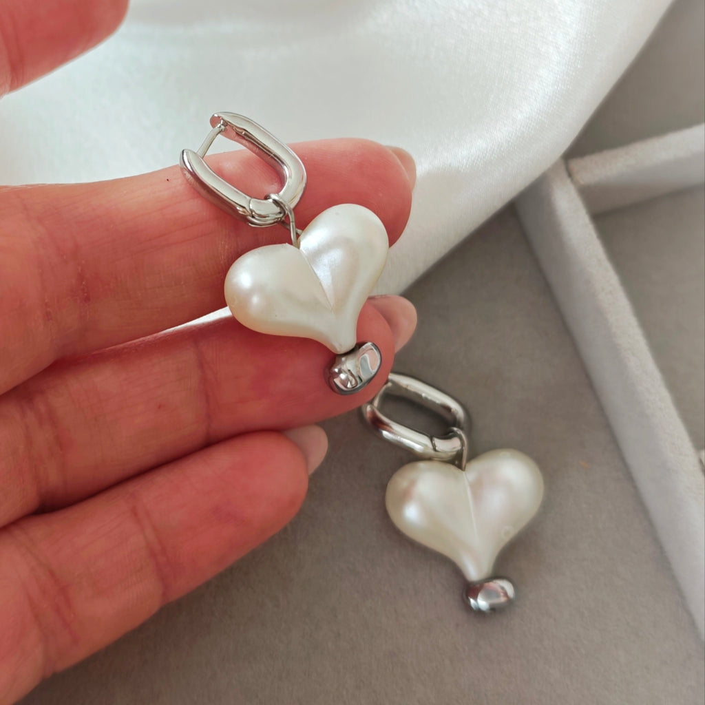 Silver hoop earrings with white pearlescent heart charms on fabric