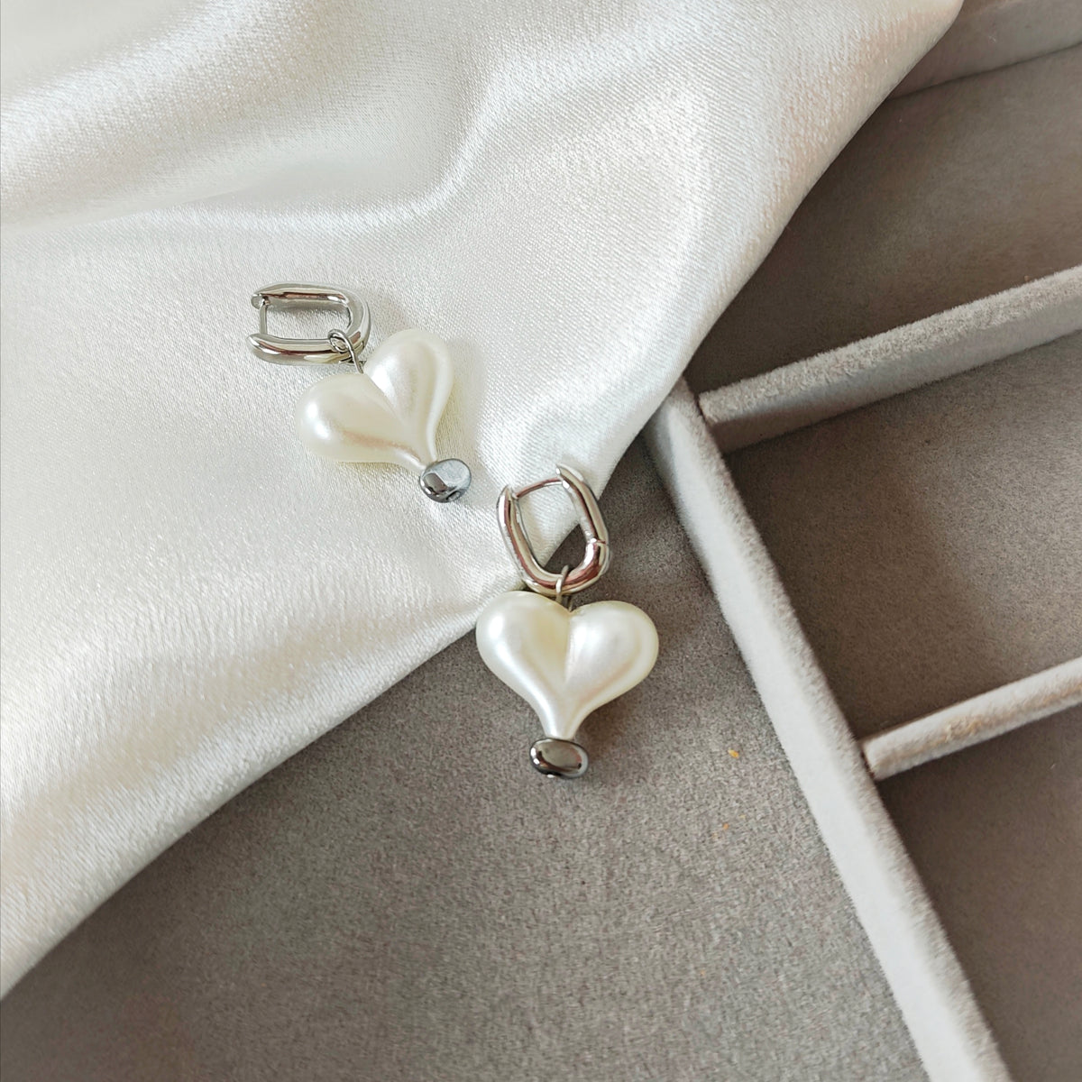Close-up of silver hoop earrings with white pearlescent heart charms