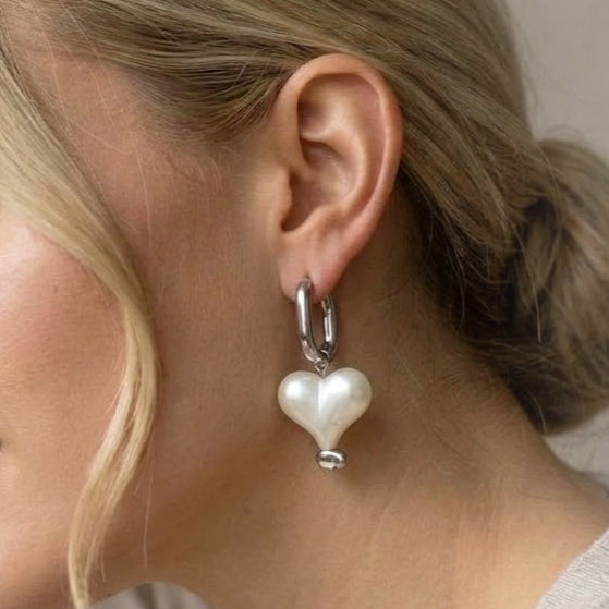 Silver hoop earring with white pearlescent heart charm worn on ear