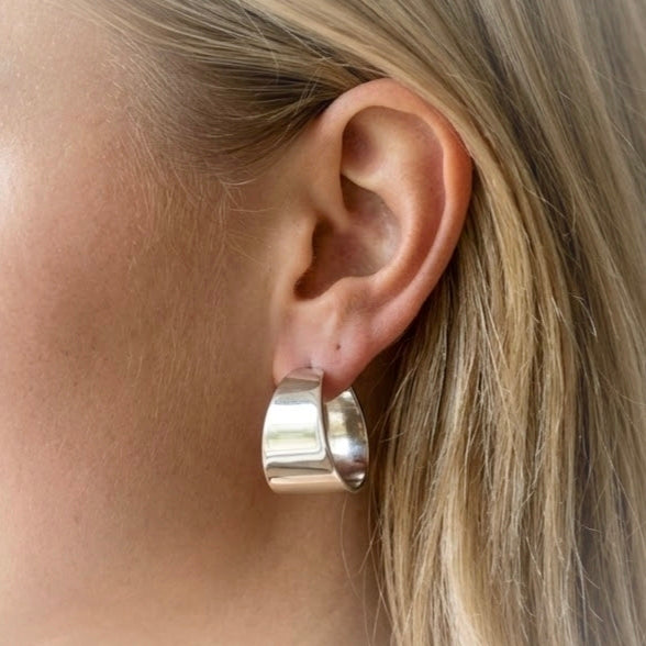 Wide polished silver-tone hoop earring worn on the ear.