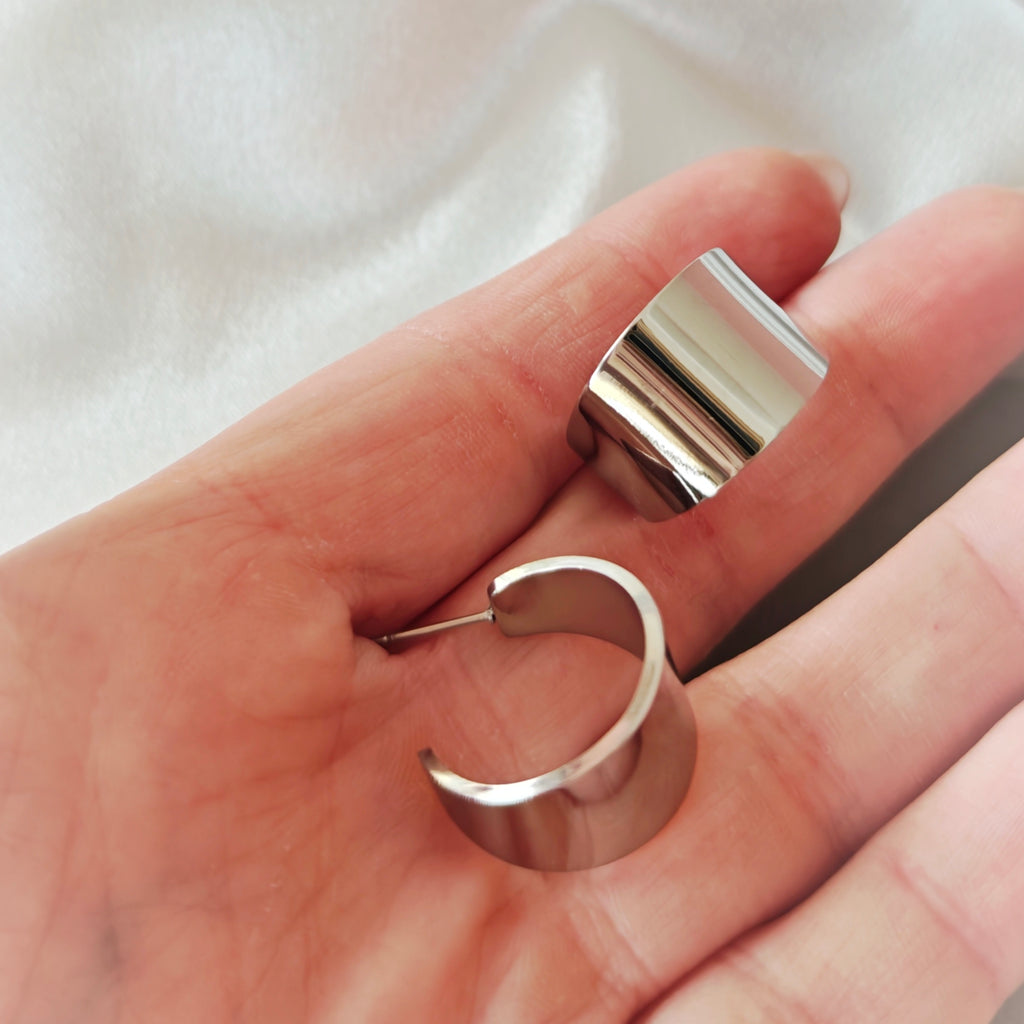 Pair of wide polished silver-tone open hoop earrings held in a hand.