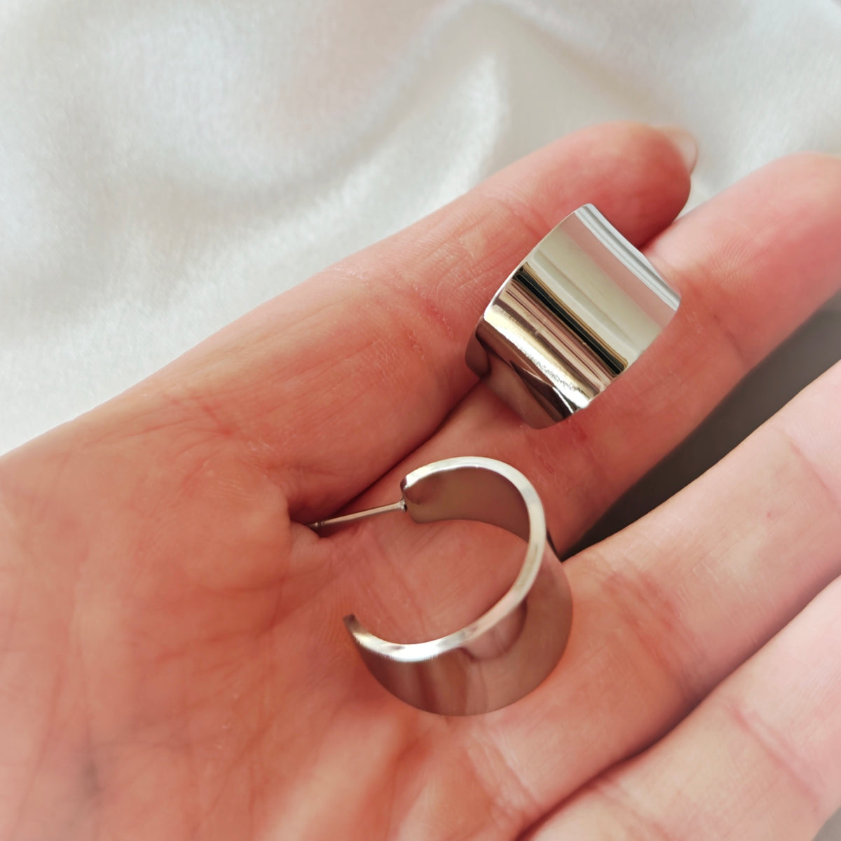 Pair of wide polished silver-tone open hoop earrings held in a hand.
