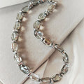 Lucent necklace with translucent grey oval crystal beads and silver-tone hematite details on a beige display.