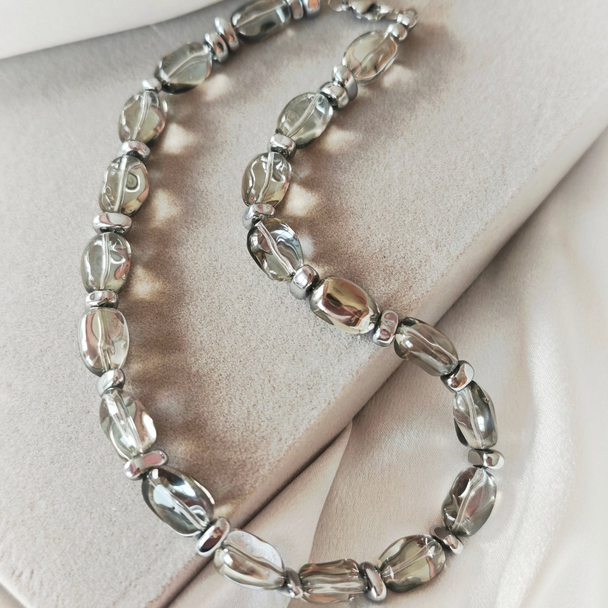 Lucent necklace with translucent grey oval crystal beads and silver-tone hematite details on a beige display.