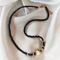 Noir Muse necklace with black crystal beads, a white pearl and gold-tone details on ivory satin.