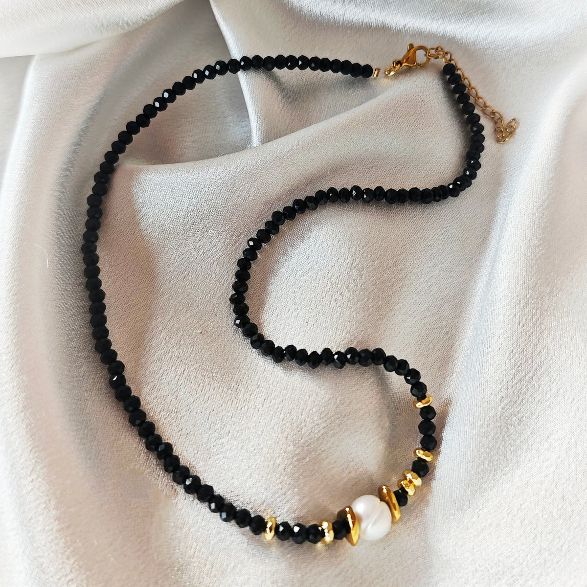 Noir Muse necklace with black crystal beads, a white pearl and gold-tone details on ivory satin.