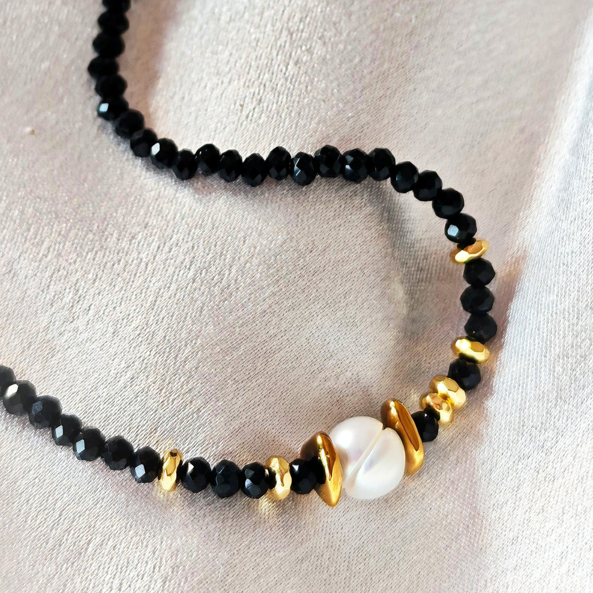 Close-up of the white pearl and gold-tone hematite details on the Noir Muse black crystal necklace.